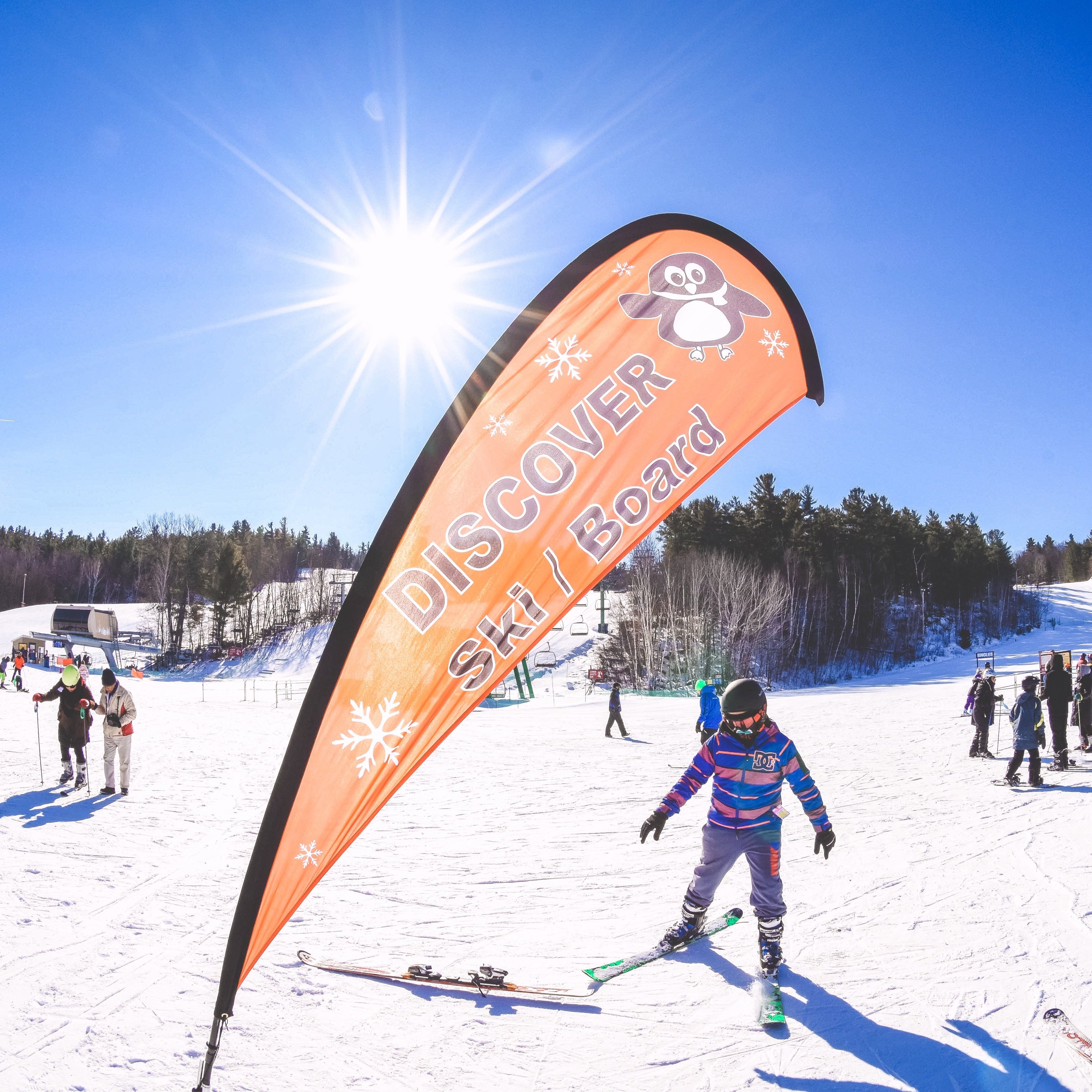 Person skiing on a snowy slope with a Discover Ski & Board banner in the foreground.