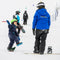 A child in a navy snowsuit and green helmet balances on a snowboard on a snowy ski slope, while an adult in a bright blue North Mountain jacket and black pants stands nearby on a snowboard.