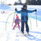 Two children on skis posing on a snowy landscape, with ski equipment and other skiers in the background.