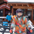 Adult participant in ski attire smiling at the camera on a snowy mountain resort grounds.