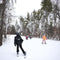 Youth ski and snowboard program with adults assisting children on a ski slope with snow-covered trees in the background.
