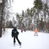 Youth ski and snowboard program with adults assisting children on a ski slope with snow-covered trees in the background.