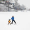An adult and a child skiing down a snow-covered slope with ski lifts in the background.