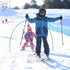 Two children on a ski resort slope, dressed in ski gear, posing with their skis and poles. The child in the foreground is smiling and extending their arms, while the other child is slightly behind and to the side, also with a happy expression.