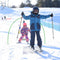 Two young children, both wearing ski gear, standing on skis and snowboards respectively, with arms raised. They are on a snow-covered slope with other skiers in the background.